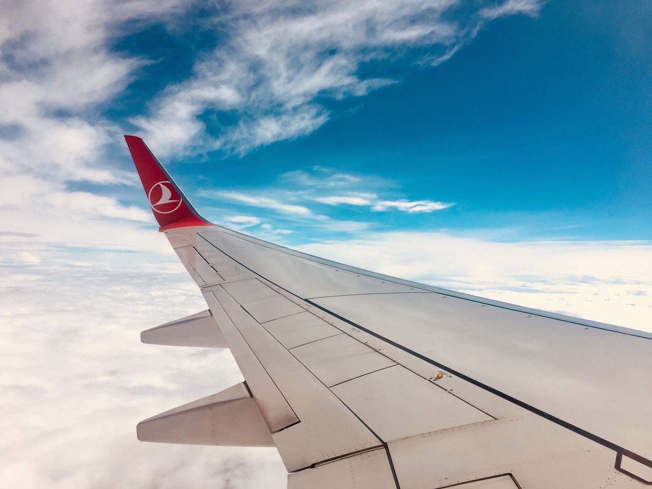 Photo of an airplane wing against a vivid blue sky and soft clouds.