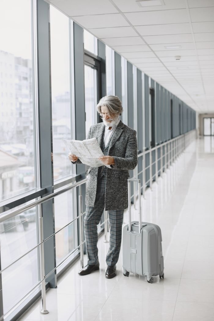 Businessman in a gray suit reading a newspaper in an airport corridor with suitcase.