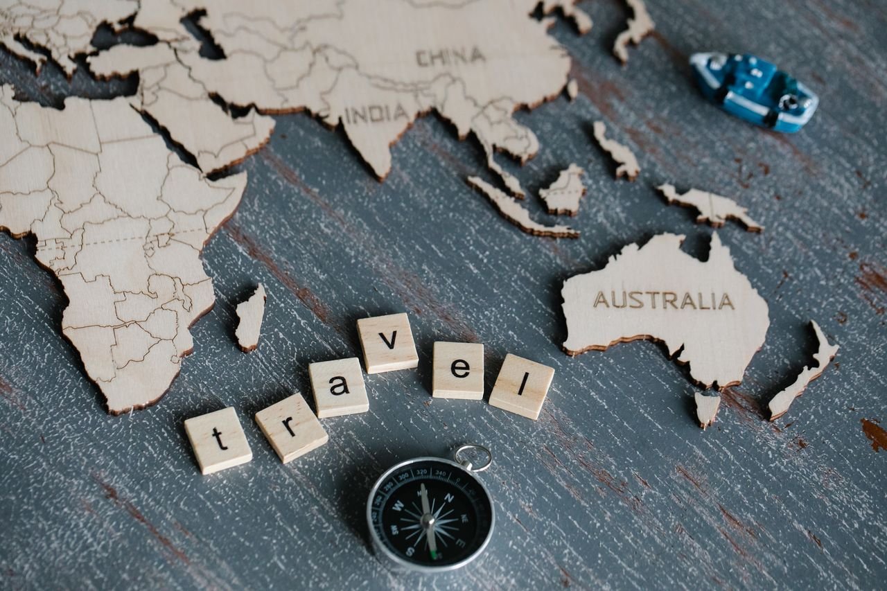 Creative travel concept featuring a wooden world map, compass, and scrabble letters spelling 'travel.'